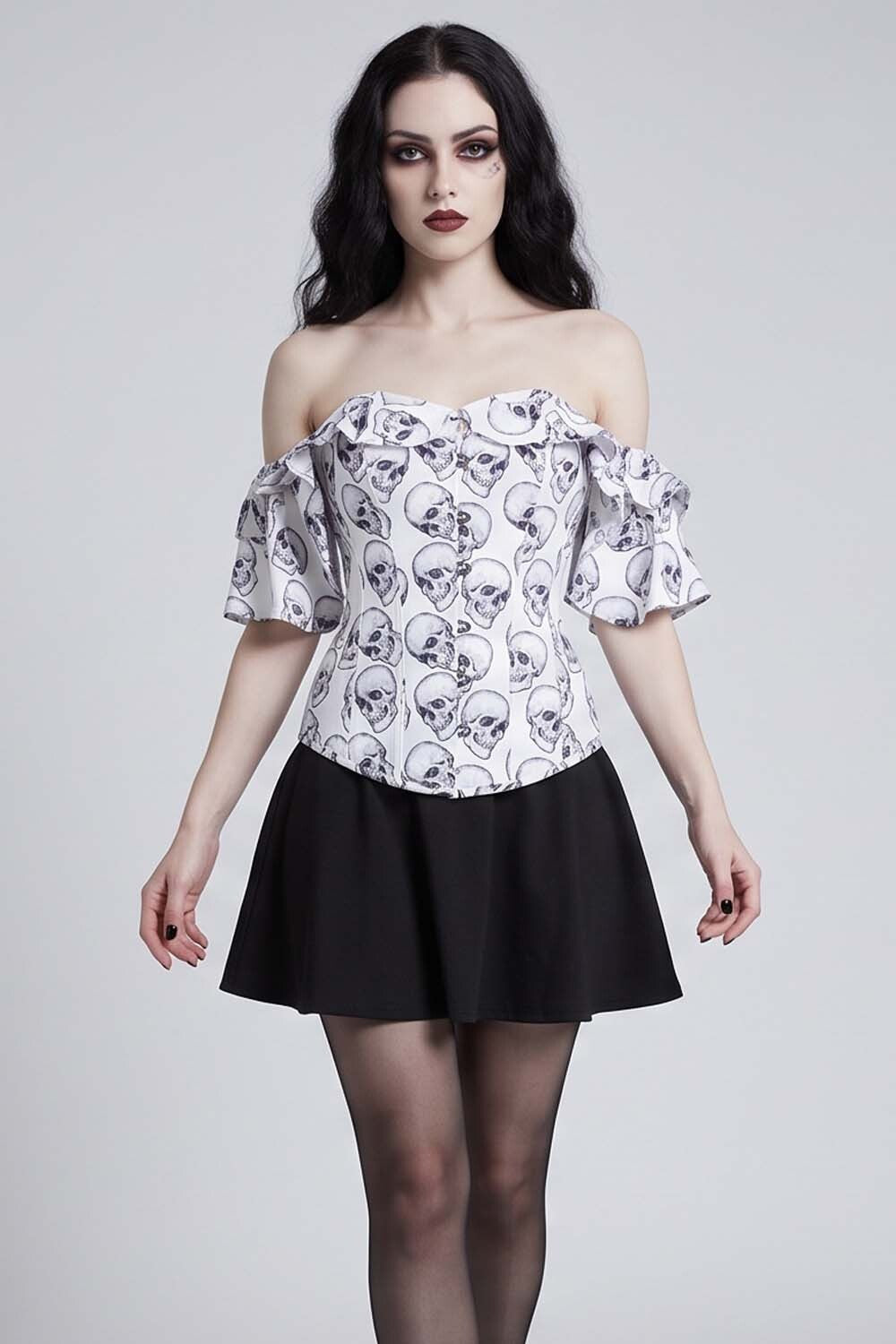 A woman modeling an Luxe Noir Corset off-the-shoulder white top with a black skull and crossbones pattern, paired with a black skirt, against a light gray studio background.