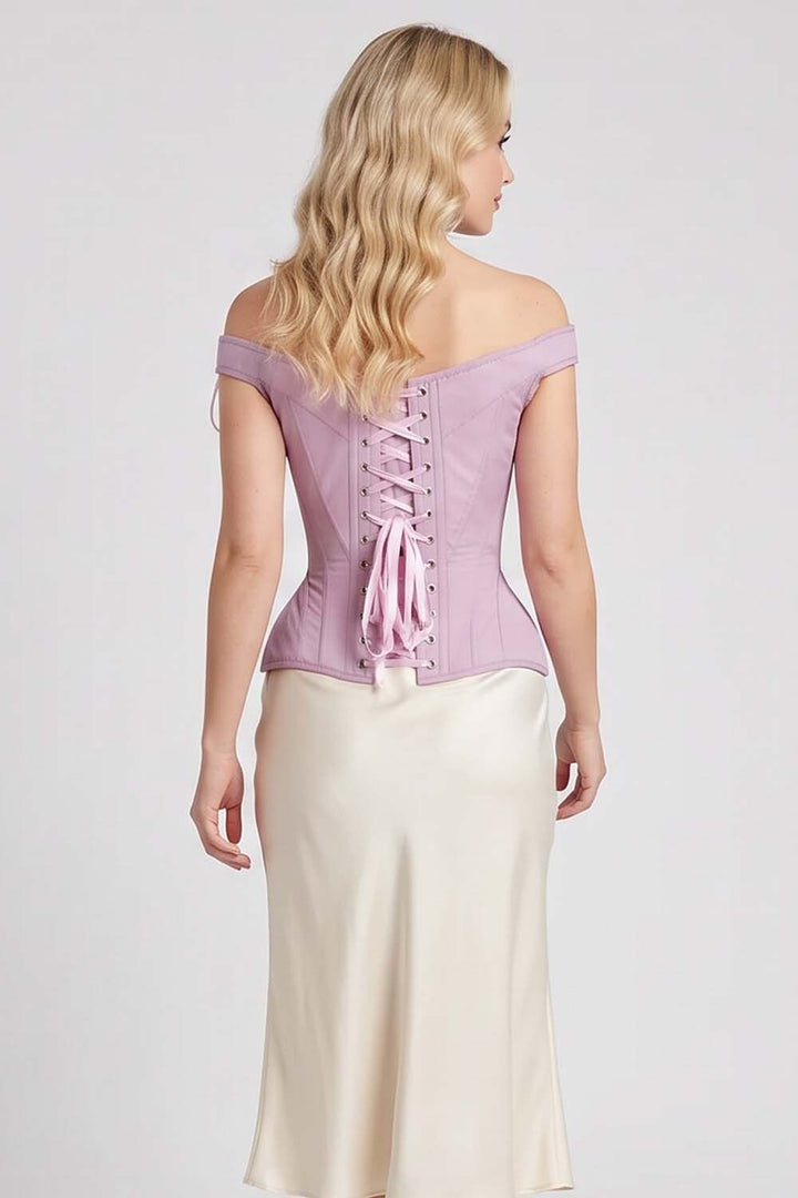 A woman shown from the back wearing a Luxe Noir Corset lavender off-the-shoulder corset top with lace-up back detailing and a cream satin skirt, against a light gray studio background.