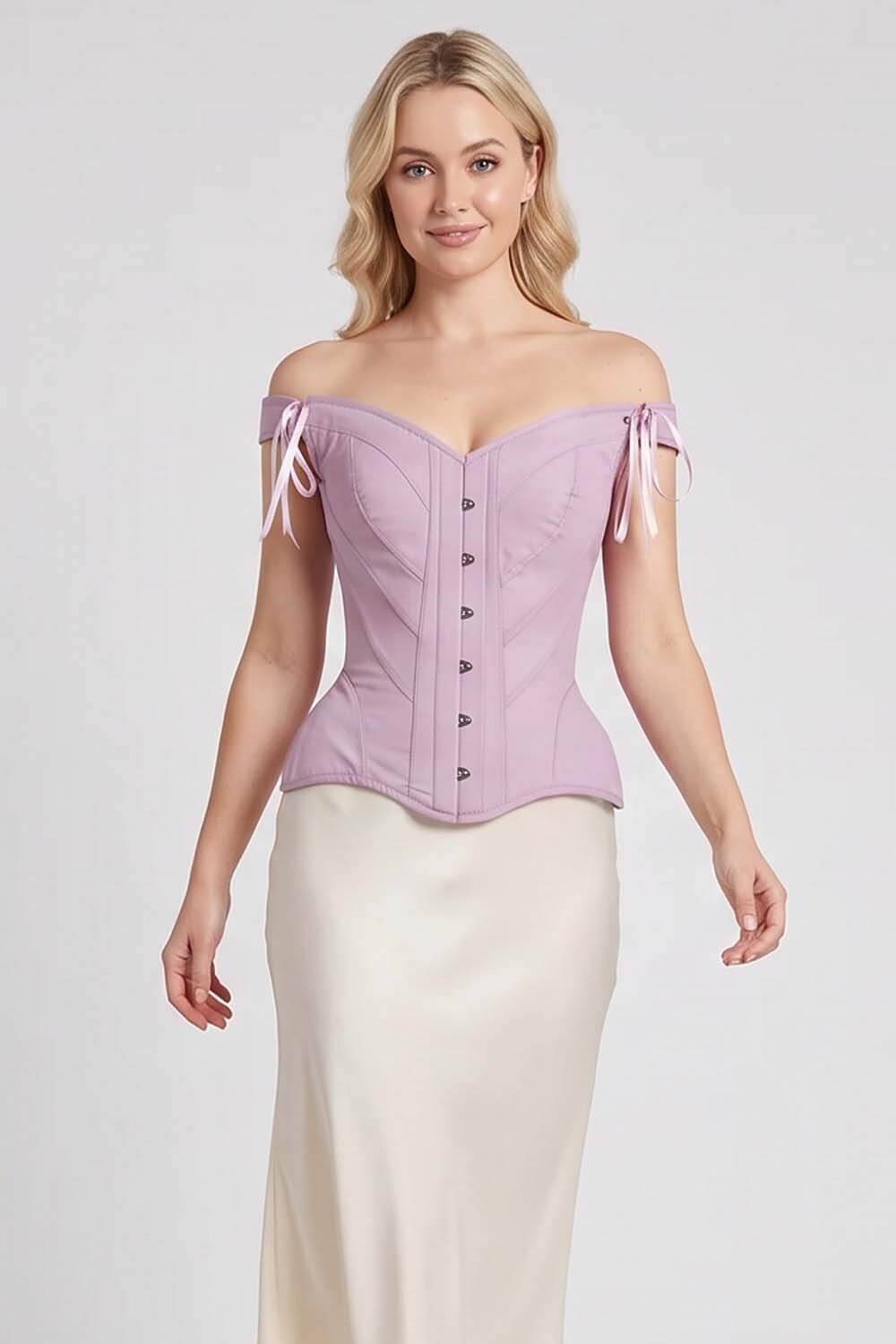 A woman modeling a Luxe Noir Corset lavender off-the-shoulder corset top with side tie details and a cream satin skirt against a light gray studio background.