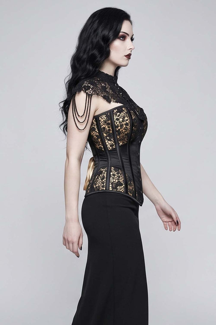 A woman modeling a  Luxe Noir Corset  black lace and gold brocade corset top paired with a long black skirt, photographed against a neutral light gray studio background.