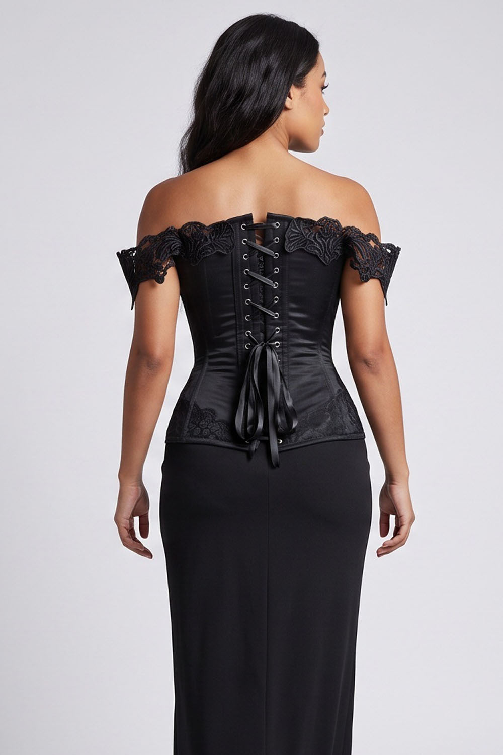 A woman shown from the back wearing a Luxe Noir black off-the-shoulder corset top with lace trim and a long black skirt against a light gray studio background.