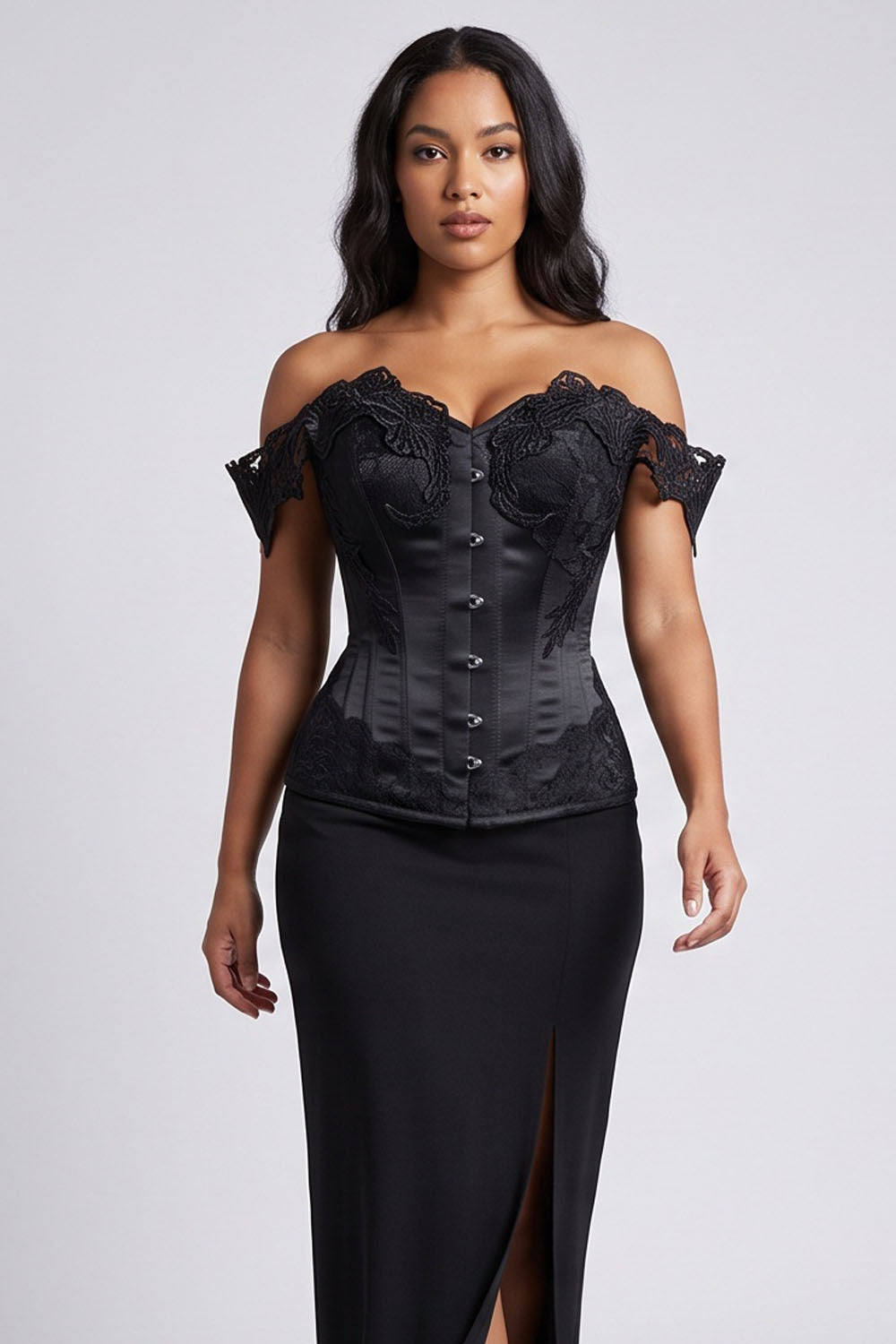 A woman modeling a Luxe Noir black off-the-shoulder corset-style top with lace and satin details, paired with a black skirt, against a light gray studio background.