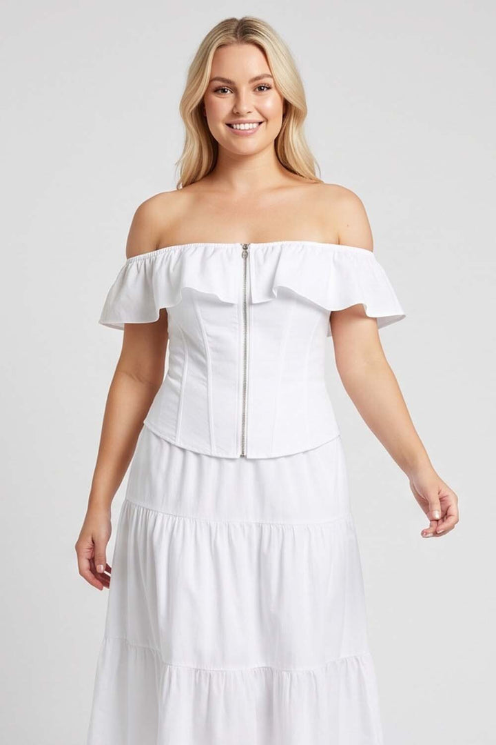 A woman modeling a LUXE NOIR CORSET white off-the-shoulder midi dress with a structured ruffled bodice, front zipper, and tiered skirt against a light gray studio background.