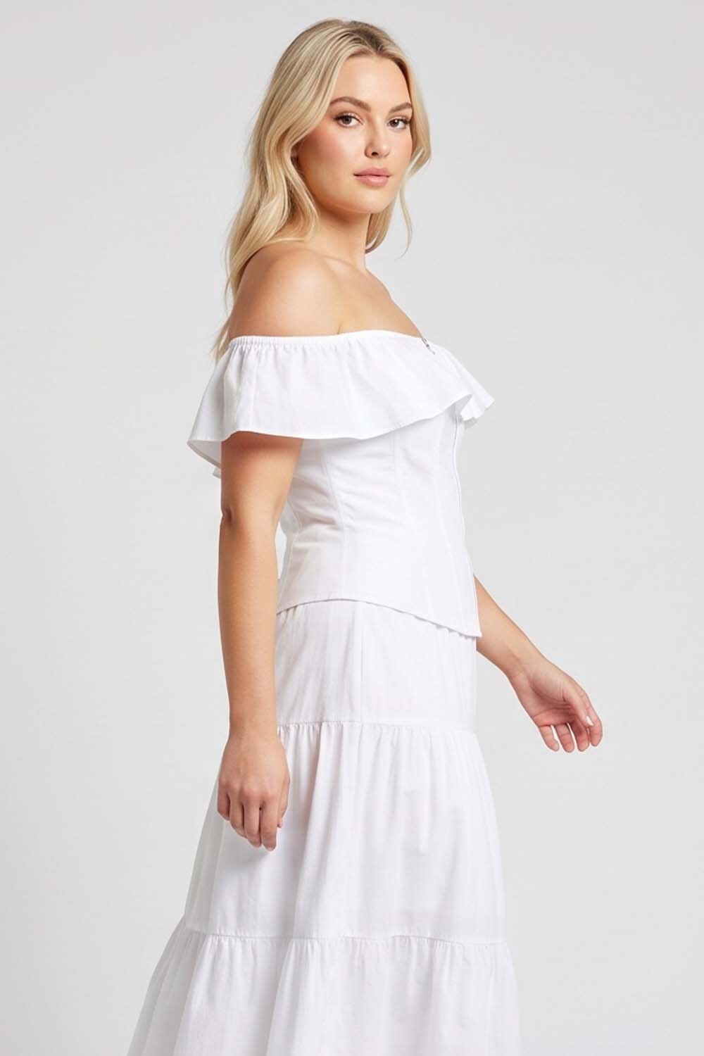 A blonde model wearing a LUXE NOIR CORSET white off-the-shoulder tiered maxi dress, shown from a side profile against a light gray studio background.