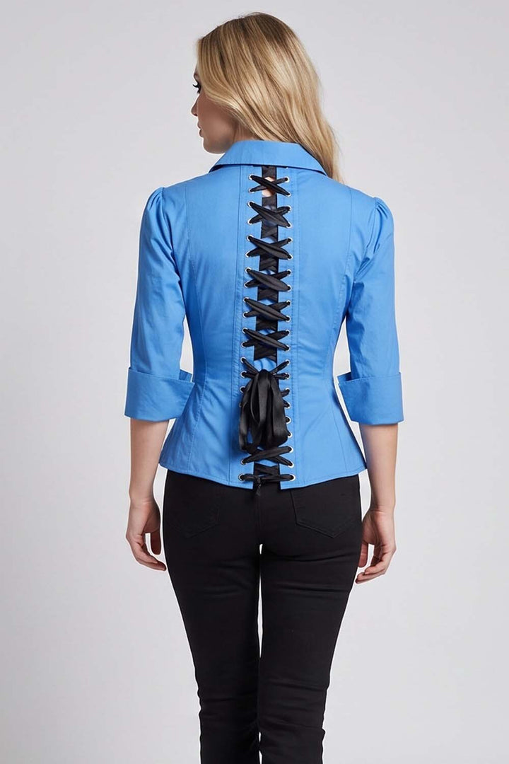 A woman viewed from the back wearing a Luxe Noir bright blue collared blouse with a prominent black lace-up detail running down the center back, paired with black pants, against a light gray studio background.