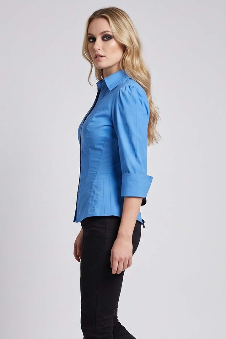 A woman modeling a Luxe Noir  bright blue button-up shirt with three-quarter sleeves and black pants, shown in a side profile against a light gray studio background.