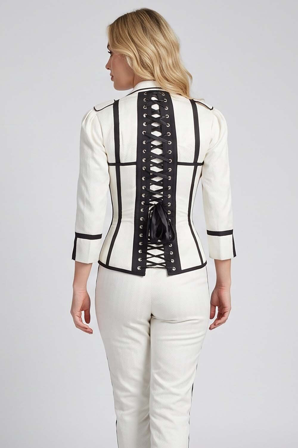 A woman shown from the back wearing a Luxe Noir structured white jacket with black trim and a lace-up back, paired with white pants, against a light gray studio background.