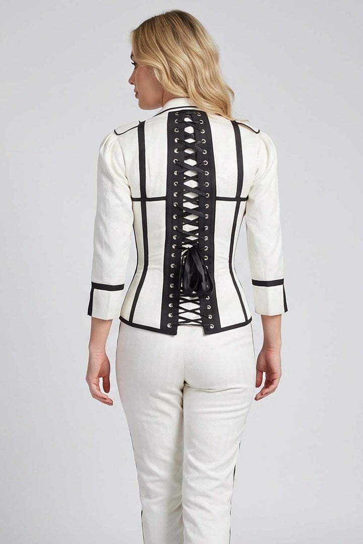 A woman shown from the back wearing a Luxe Noir structured white jacket with black trim and a lace-up back, paired with white pants, against a light gray studio background.