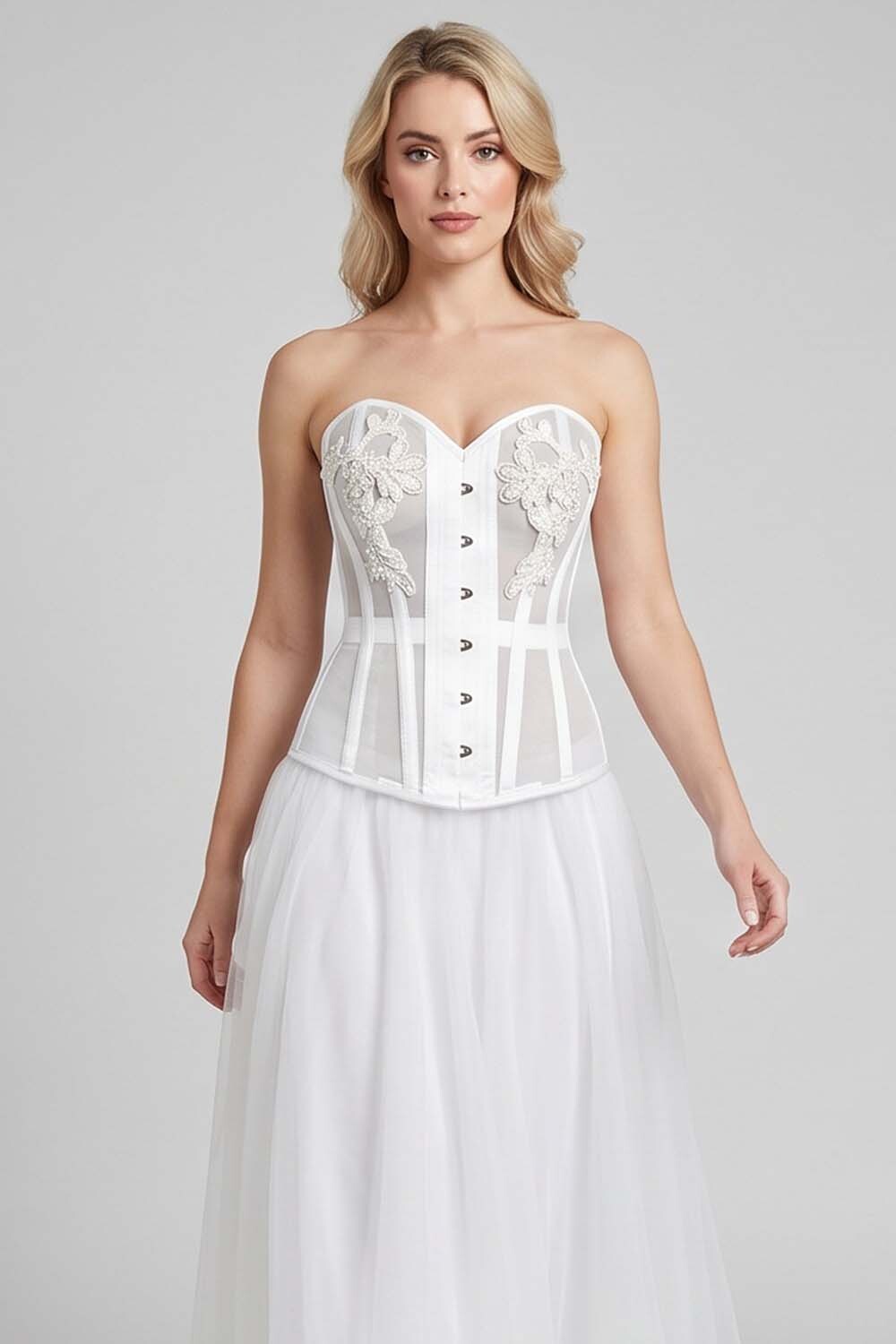 A woman modeling a white LUXE NOIR CORSET strapless corset-style top with floral lace applique and a long flowing tulle skirt against a light gray studio background.
